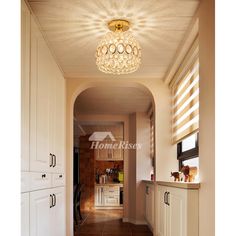 a hallway leading to a kitchen with white cabinets and brown tile on the floor is lit by a round light fixture