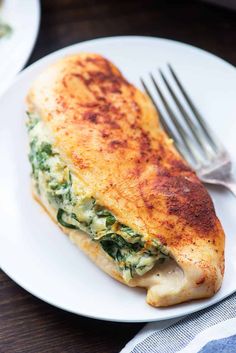 a white plate topped with an omelet covered in cheese and spinach next to a fork