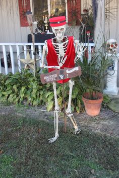 a skeleton dressed up as a man holding a sign in front of a house with potted plants