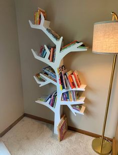 a white tree shaped book shelf next to a lamp in a room with carpeted flooring