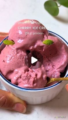 a bowl filled with pink ice cream on top of a table next to two hands