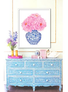 a blue and white vase with pink flowers on it sitting on top of a dresser