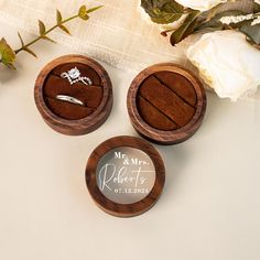 three wooden boxes with wedding rings in them on a table next to flowers and a white rose