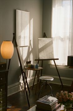 an easel sitting in front of a window next to a table with a lamp on it