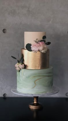 a three - tiered cake with gold and green frosting on a marble stand