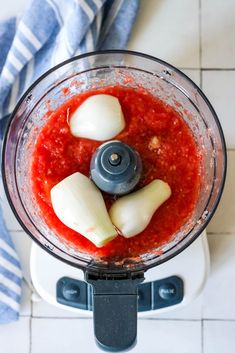 an overhead view of a food processor with red sauce and onions in the blender