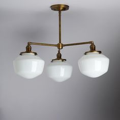 three white glass shades hang from an antique brass chandelier