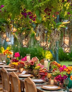 an outdoor dining table set with flowers, candles and vases hanging from the ceiling