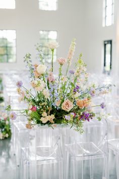 an arrangement of flowers is placed on the back of clear chairs at a wedding reception