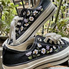 two black and white shoes with flowers on them sitting next to each other in front of some plants