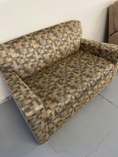 a couch sitting on top of a cement floor next to a wall with a brown and tan checkered design