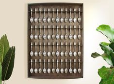 a wall hanging with spoons on it next to a potted plant and green leaves