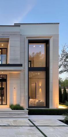 a modern house with large windows and white walls at dusk, as seen from the driveway