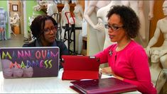 two women sitting at a table with laptops and mannequins behind them