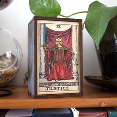 a tarot card sitting on top of a wooden shelf next to a potted plant