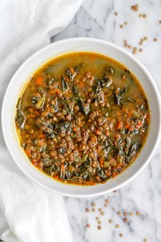 a white bowl filled with lentula and spinach soup on top of a marble counter