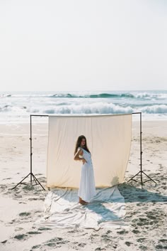 a woman standing on top of a sandy beach next to an empty white sheet covered chair