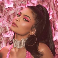 a woman with long hair wearing large hoop earrings and a pink dress is standing in front of money bills