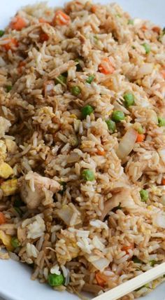 rice with peas and carrots in a white bowl next to chopsticks on a table