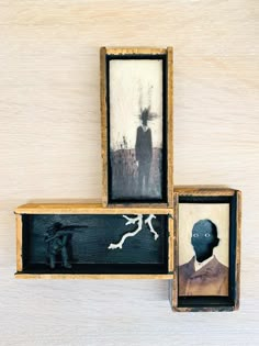 three wooden frames with paintings on them and one has a man's head in the middle