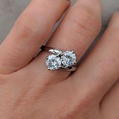 a woman's hand with two engagement rings on her left and the other hand holding an engagement ring