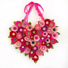 a heart shaped origami flower arrangement hanging on a wall with a pink ribbon