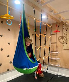 a little boy is playing in a hammock suspended from the ceiling with ropes