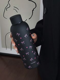 a woman holding a black and pink water bottle in front of a wall with a drawing on it