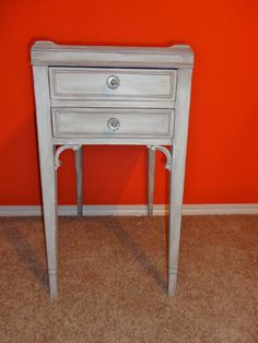 a small white table with two drawers against an orange wall and carpeted flooring