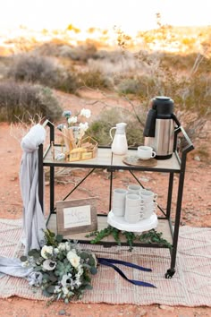 a table with coffee cups and plates on it in the middle of an open field