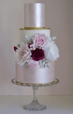 a three tiered wedding cake with pink and white flowers on the top, sitting on a pedestal