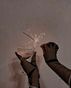 two hands holding a wine glass with a sparkler in the middle, and another hand reaching for it