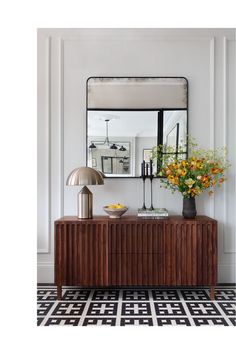 a large mirror sitting above a wooden cabinet next to a vase with flowers on it