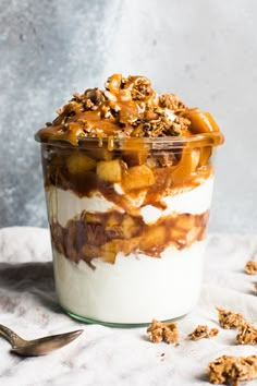 a dessert in a glass on top of a white table cloth with spoons next to it