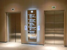 three elevators with signs on them in an empty room at the end of two walls