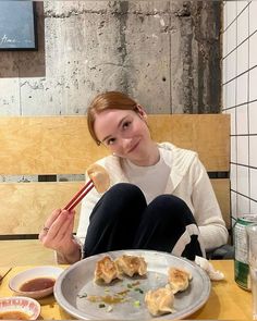 a woman sitting at a table with food on it and chopsticks in her hand