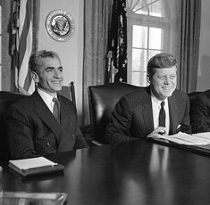 three men sitting at a table in front of the white house with papers and pen