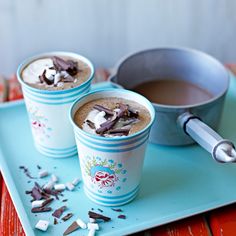 three cups of hot chocolate and marshmallows on a blue tray