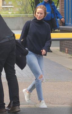 a woman is walking down the street with her hand in her pocket and another man behind her