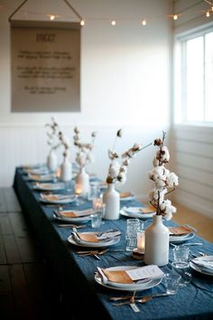 the table is set with blue linens and white vases filled with flowers, silverware, and candles