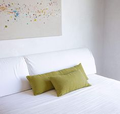 a bed with two green pillows on top of it next to a painting hanging above the headboard