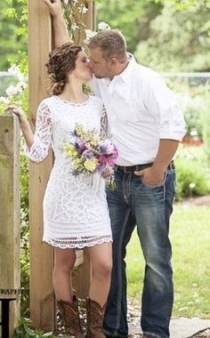 a man and woman standing next to each other in front of a wooden structure with flowers on it