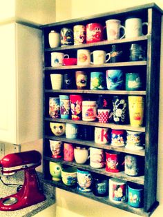 a shelf filled with lots of cups next to a red mixer on top of a counter