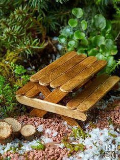 a small wooden bench sitting on top of snow covered ground next to trees and plants