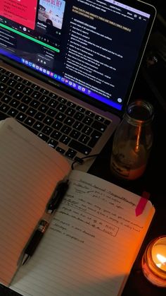 an open notebook sitting on top of a laptop computer next to a candle and pen