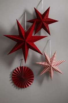 three red paper stars hanging from strings on a gray wall next to a pinwheel