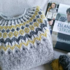 a knitted sweater next to a book and knitting needles