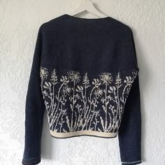 a blue sweater with white flowers on it hanging from a hanger against a wall