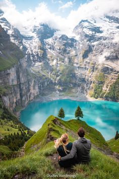 a man and woman sitting on top of a mountain looking at a lake in the mountains