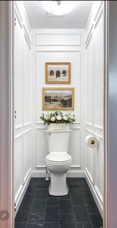 a white toilet sitting inside of a bathroom next to a doorway with pictures on the wall